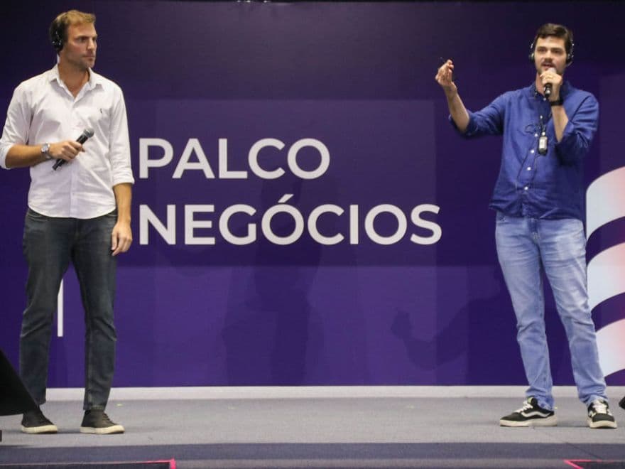 Agente de IA: Alex e Jeferson do Grupo OLX, no Palco Negócios durante conferência, discutindo tendências do setor e o impacto do agente de IA.