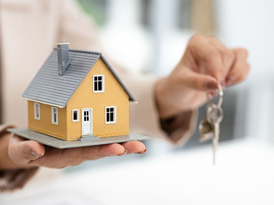 Pessoa segurando uma casinha decorativa e chaves.