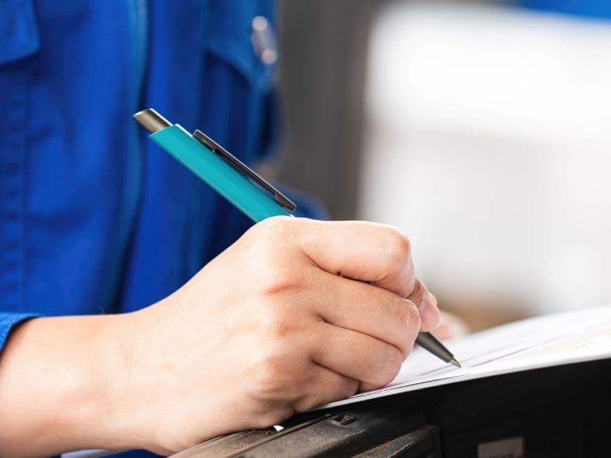 Profissional em uniforme azul preenche um formulário com caneta azul, representando a documentação e aprovação necessária para a emissão do AVCB