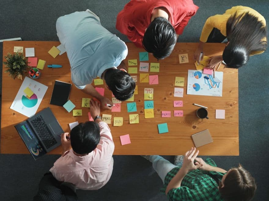 Equipe de profissionais planejando ações em mesa com gráficos e post-its coloridos, ilustrando estratégias criativas para captação de leads