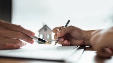 Mãos segurando canetas acima de um papel enquanto é explicado sobre a certidão de ônus real.