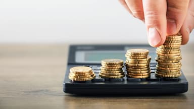 Pessoa empilhando moedas sob calculadora.