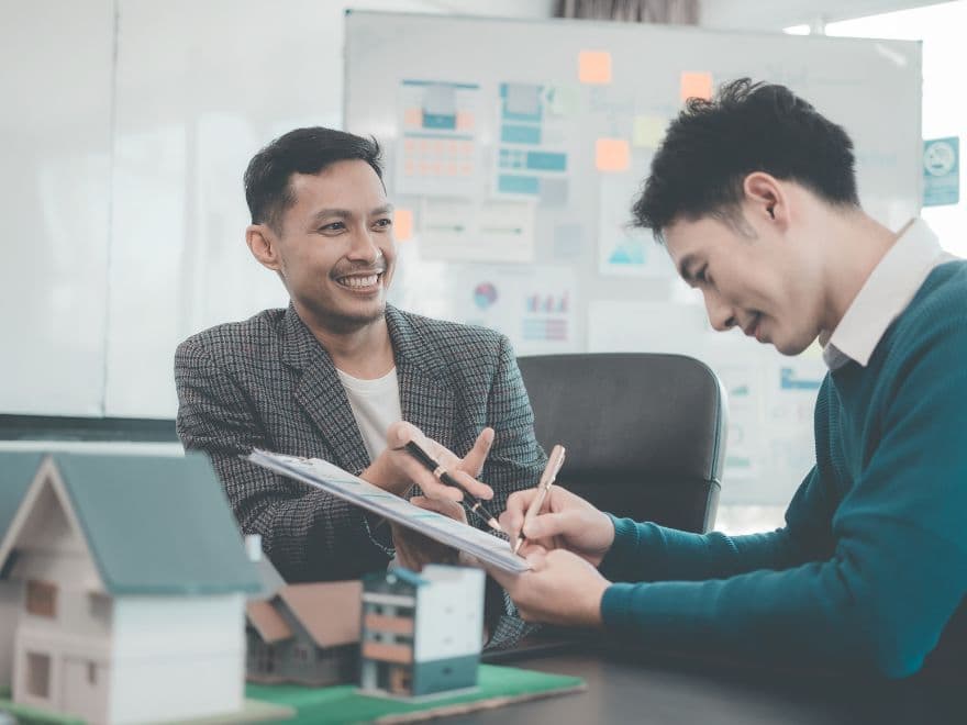 Corretor de imóveis e cliente assinando contrato de compra e venda, garantindo a conformidade técnica da obra com base no memorial descritivo registrado em cartório. 