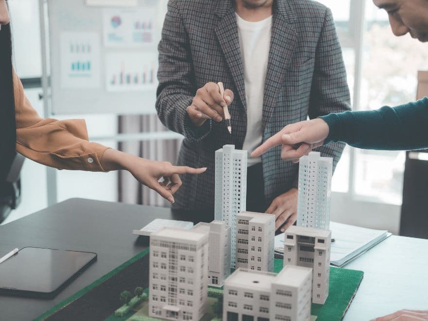 Incorporadores e corretores em reunião estratégica analisando maquetes de edifícios de alto padrão para validar as especificações contidas no memorial descritivo do empreendimento.