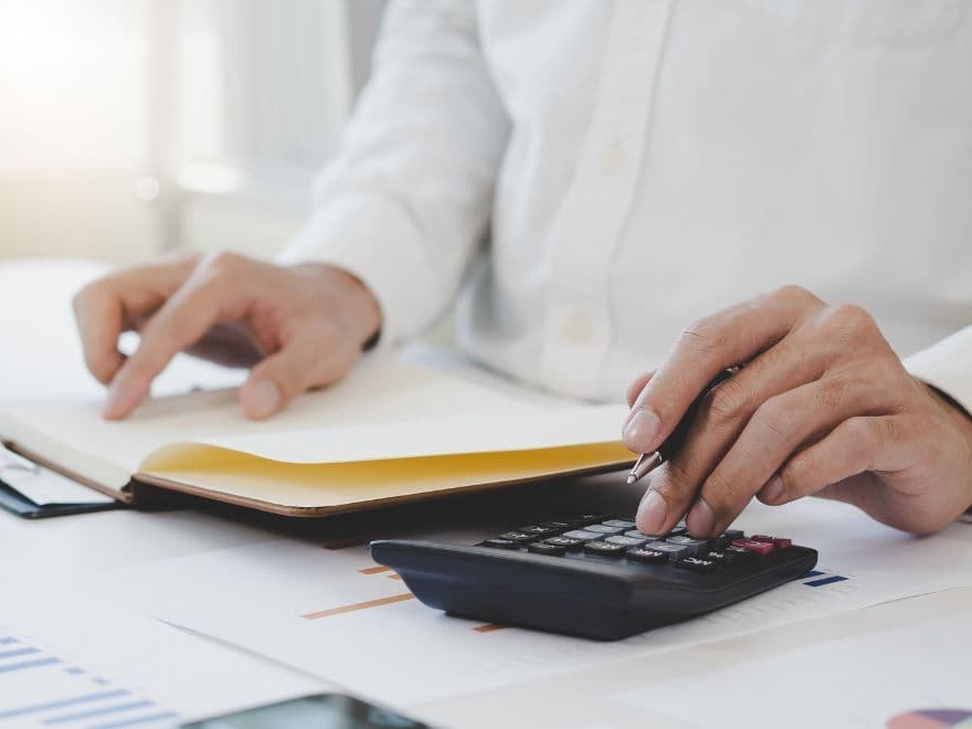 Profissional de incorporação imobiliária utilizando calculadora e notebook para simular custos de outorga onerosa.