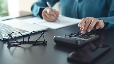 Profissional de incorporação imobiliária utilizando calculadora e notebook para simular custos de outorga onerosa.