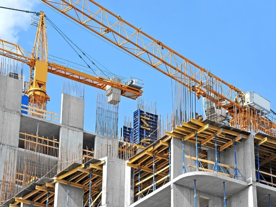 Vista de um canteiro de obras de grande porte com guindastes amarelos operando em estruturas de concreto armado, exemplificando a modernização e os padrões de segurança exigidos pela certificação PBQP-H.