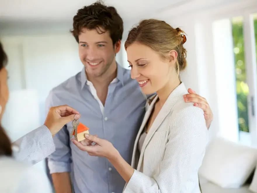 Corretora entregando as chaves de um imóvel para um casal de compradores após verificação de débitos e propter rem.