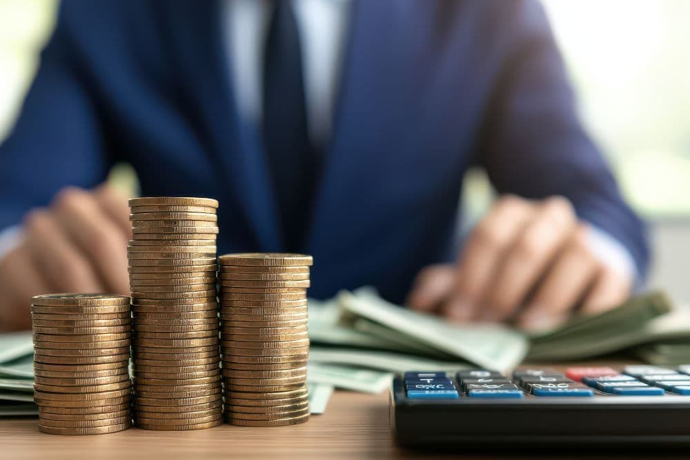 Executivo ao fundo com pilhas de moedas e cédulas em primeiro plano, simbolizando o aporte de capital e a distribuição de lucros em uma SCP imobiliária.