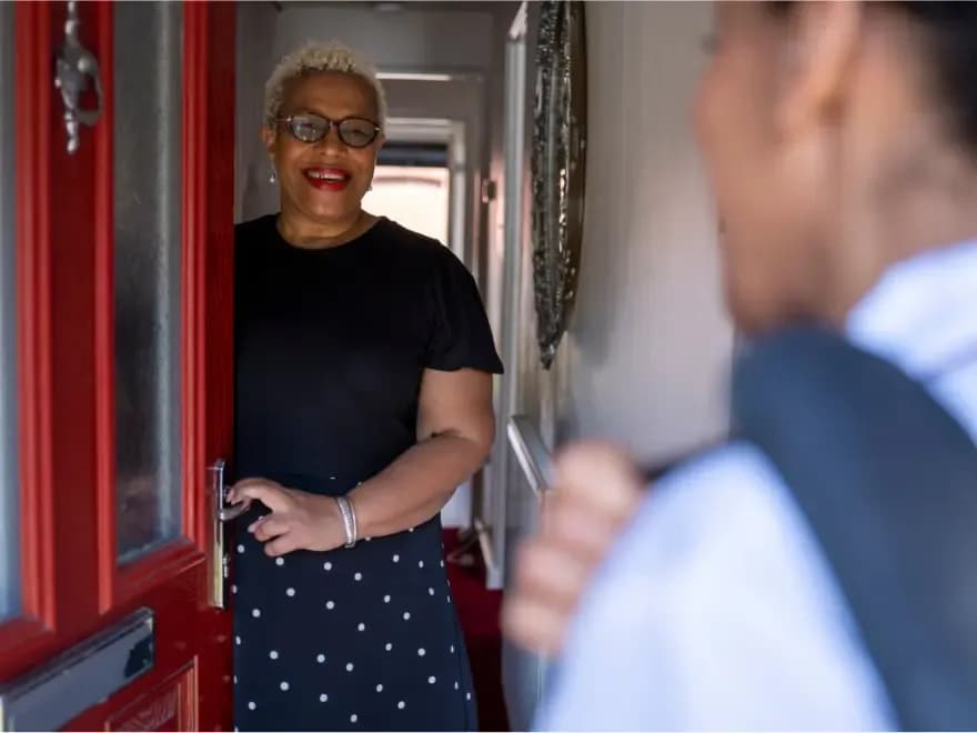 Mulher sorrindo atende porta de casa para visitante, representando negociação imobiliária presencial com atenção aos riscos de golpes na venda de imóveis e segurança no processo.