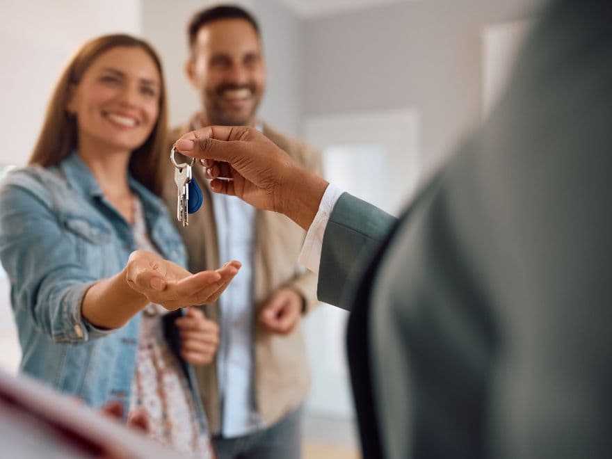 Duas pessoas sorridentes recebendo as chaves de sua casa.